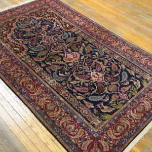 Dark navy and deep red rug with intricate floral and bird patterns lying on light wood flooring.
