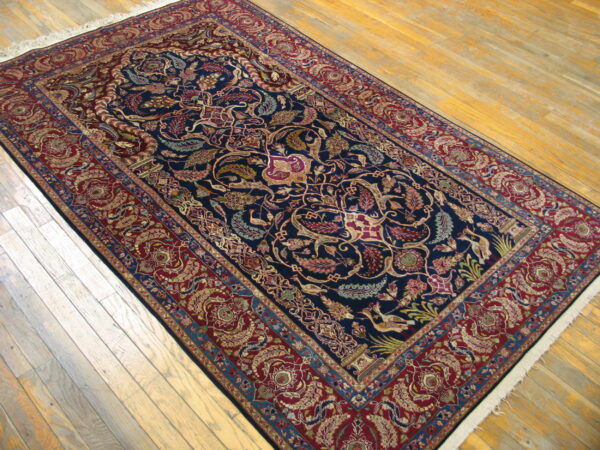 Dark navy and deep red rug with intricate floral and bird patterns lying on light wood flooring.