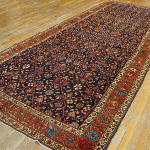 Detailed navy rug with red lattice floral motifs rests on distressed yellow hardwood plank flooring.
