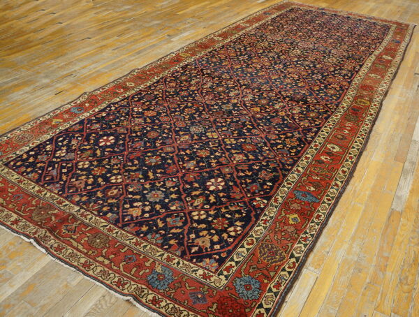 Detailed navy rug with red lattice floral motifs rests on distressed yellow hardwood plank flooring.
