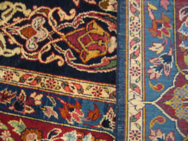 Close detail showing navy, red, and cream scrolling high-pile rug meeting a bright blue geometric woven pattern.