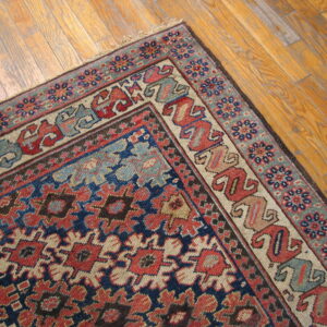 A densely patterned rug in navy, red, and light blue rests diagonally on a warm wood floor.