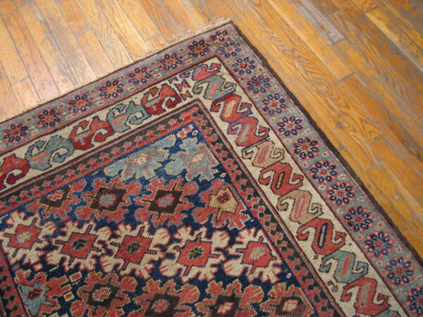 A densely patterned rug in navy, red, and light blue rests diagonally on a warm wood floor.