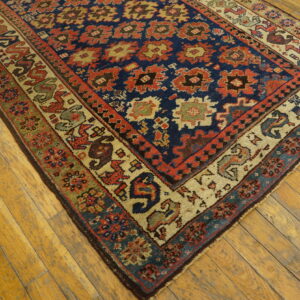 Multicolor geometric rug with a dark blue field and complex borders rests on light wooden floorboards.