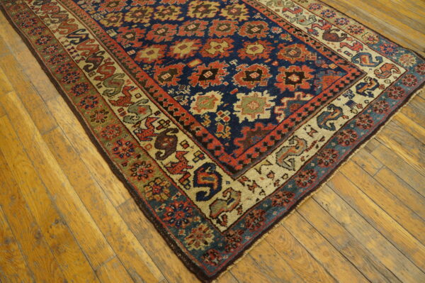 Multicolor geometric rug with a dark blue field and complex borders rests on light wooden floorboards.