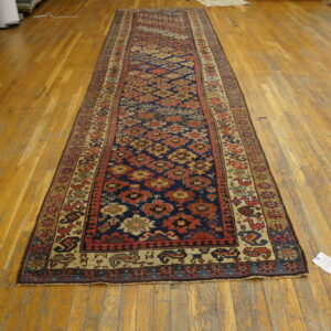 A navy and red geometric runner rug sits on honey-toned hardwood floors beside rolled storage items.