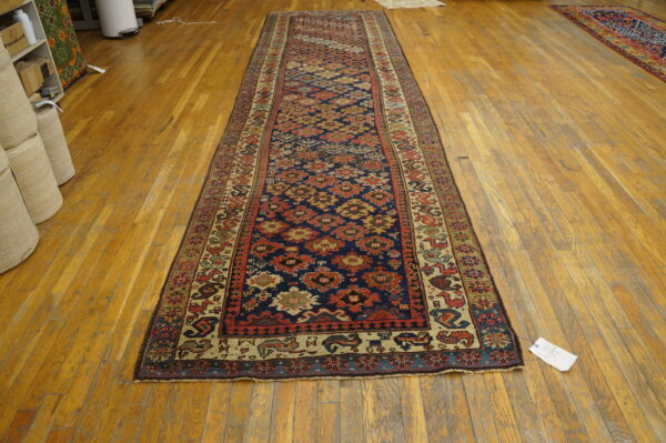 A navy and red geometric runner rug sits on honey-toned hardwood floors beside rolled storage items.