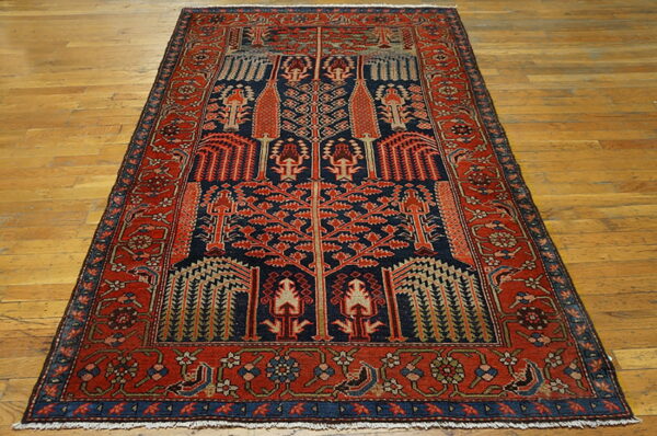 Navy and rust red rug featuring a detailed geometric tree of life pattern rests on light hardwood flooring.