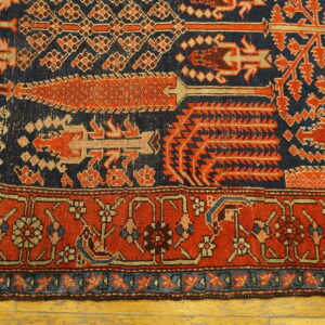 Intricate rug in navy blue and terracotta red displaying geometric patterns and a detailed floral border on wood.