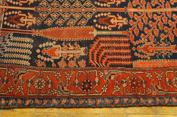 Intricate rug in navy blue and terracotta red displaying geometric patterns and a detailed floral border on wood.
