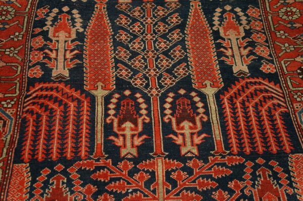 Detailed view of a low-pile rug with intricate red and cream geometric patterns on a dark navy blue background.