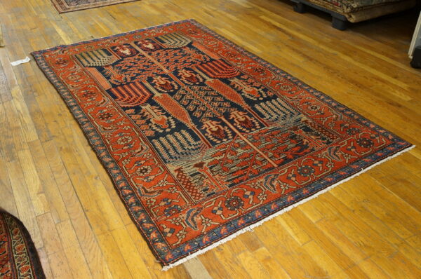 Detailed traditional rug in red-orange and navy blue on a glossy wooden floor.