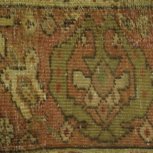 Textured close-up showing stylized geometric motifs in rust, olive green, and golden yellow on a low pile.