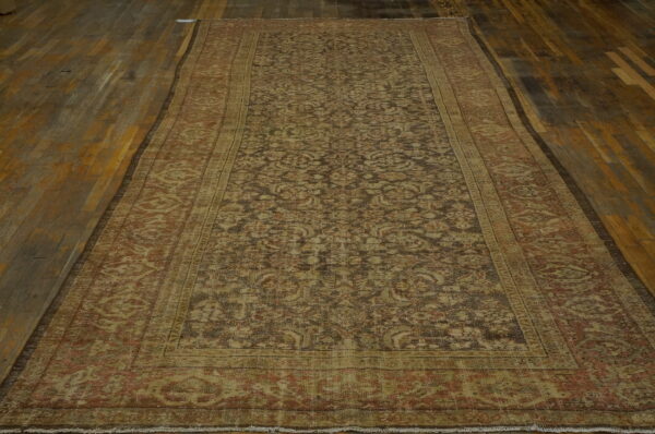 Faded long runner with dark floral motifs and wide beige borders rests on distressed wood planks.
