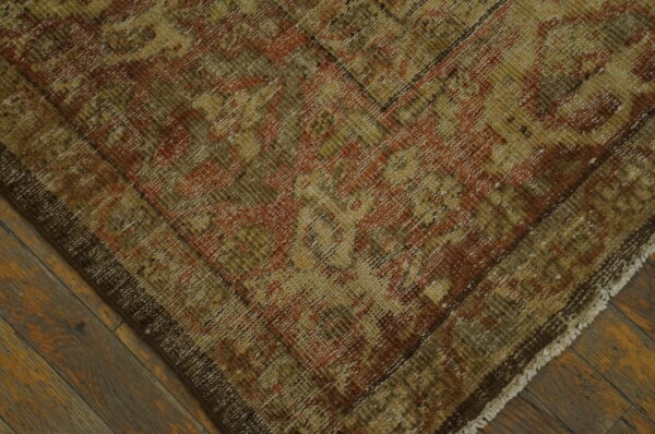 Low-pile rug featuring distressed patterns in gold, olive, and rust over dark wooden planks.