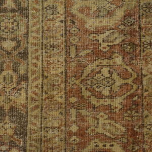 Muted, low-pile rug displaying traditional patterns in rust and tan colors, lying on wood flooring.
