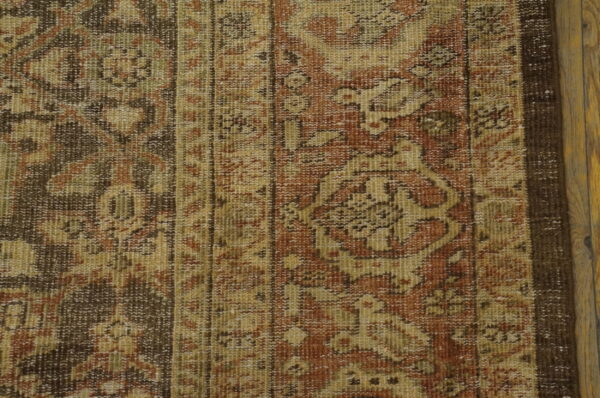 Muted, low-pile rug displaying traditional patterns in rust and tan colors, lying on wood flooring.