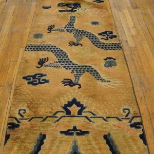 Golden runner rug with dark blue dragon patterns and pink clouds displayed on light wood plank flooring.