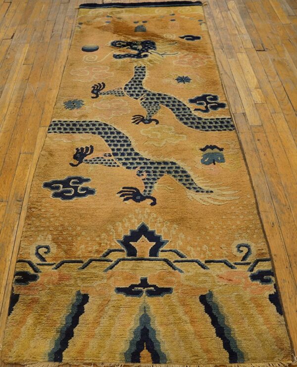 Golden runner rug with dark blue dragon patterns and pink clouds displayed on light wood plank flooring.