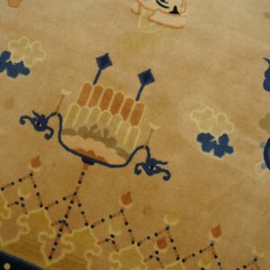 Close-up of a low pile tan rug with stylized blue, orange, and gold traditional patterns.