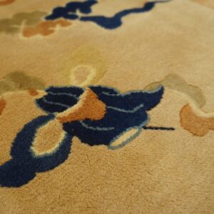 Close-up shows a tan rug with medium pile and abstract designs in navy, terracotta, and olive green.