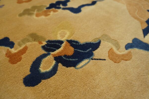 Close-up shows a tan rug with medium pile and abstract designs in navy, terracotta, and olive green.