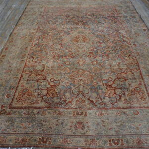 Large, ornate low-pile rug featuring muted red and blue tones rests on distressed grey wooden flooring.