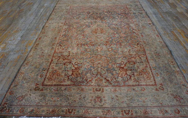 Large, ornate low-pile rug featuring muted red and blue tones rests on distressed grey wooden flooring.