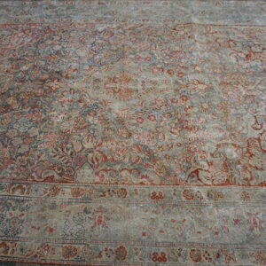 Distressed low-pile rug with complex traditional red and blue floral patterns and multiple borders on wood planks.