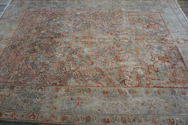 Distressed low-pile rug with complex traditional red and blue floral patterns and multiple borders on wood planks.