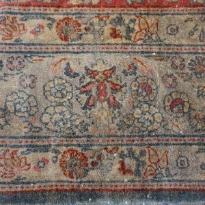 Close-up of a distressed rug border showing faded beige, red, and navy floral traditional patterns.