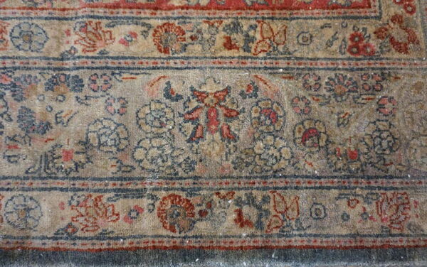 Close-up of a distressed rug border showing faded beige, red, and navy floral traditional patterns.