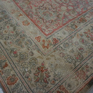 Beige and faded rose traditional rug border with fringe resting on rustic wood flooring.