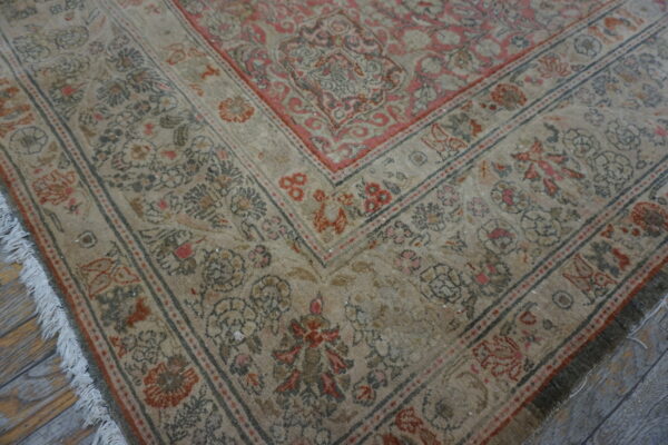 Beige and faded rose traditional rug border with fringe resting on rustic wood flooring.