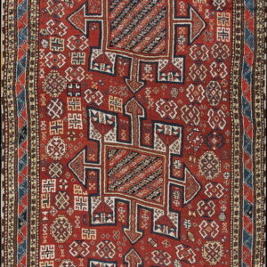 A vertical red rug featuring large geometric blue and cream medallions and dense tribal motifs.