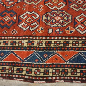 Rustic red, blue, and cream rug with geometric medallions and dense patterned borders visible over distressed wood.