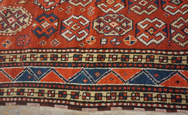 Rustic red, blue, and cream rug with geometric medallions and dense patterned borders visible over distressed wood.
