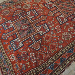 A rust red geometric tribal rug featuring blue, cream, and tan geometric patterns on a wood floor.