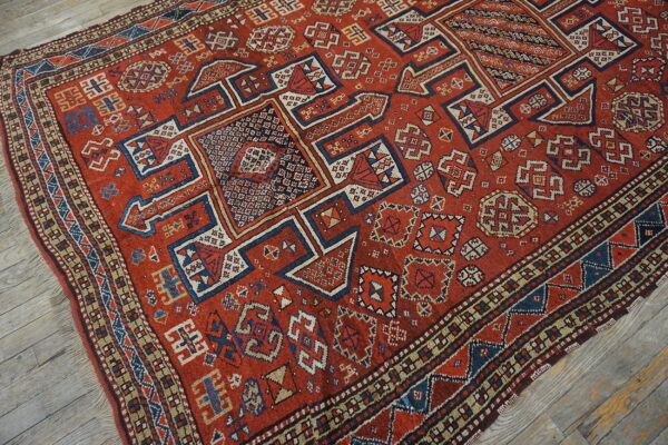 A rust red geometric tribal rug featuring blue, cream, and tan geometric patterns on a wood floor.
