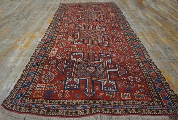 Geometric red runner rug with blue and tan central medallions and multiple borders on wood planks.
