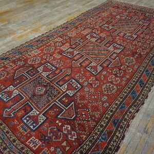 Geometric runner rug in rust red, dark blue, and tan rests upon worn, distressed wooden floorboards.