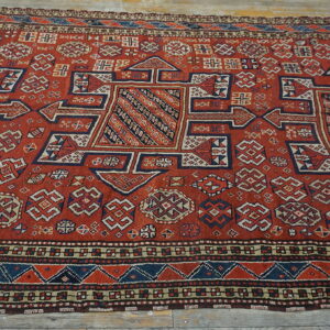 Low-pile red rug with dense geometric patterns in blue and cream laid across weathered wood planks.