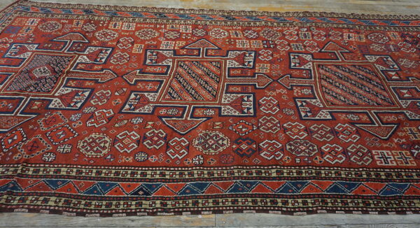 Low-pile red rug with dense geometric patterns in blue and cream laid across weathered wood planks.