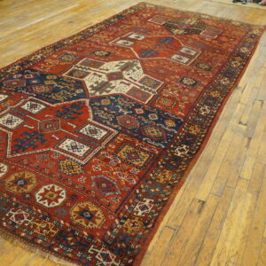 Low-pile geometric rug in red, navy, and cream colors resting on light, distressed wood floors.