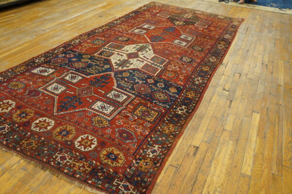 Low-pile geometric rug in red, navy, and cream colors resting on light, distressed wood floors.