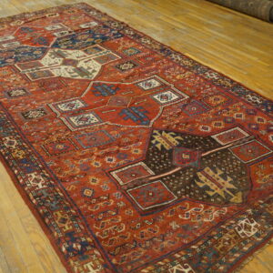 Low-pile red rug with complex blue and brown tribal geometric patterns rests on light hardwood planks.