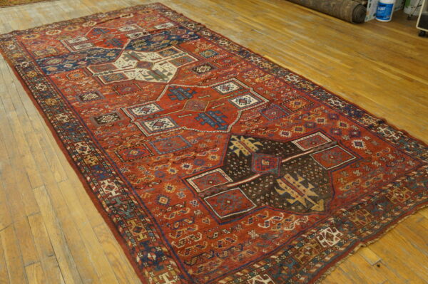 Low-pile red rug with complex blue and brown tribal geometric patterns rests on light hardwood planks.