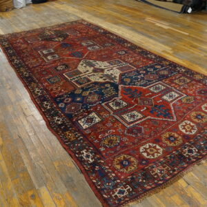Red and navy tribal rug featuring geometric designs covers a worn wooden floor.