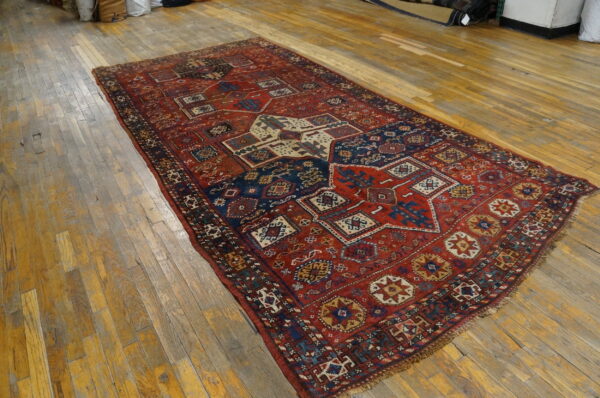 Red and navy tribal rug featuring geometric designs covers a worn wooden floor.