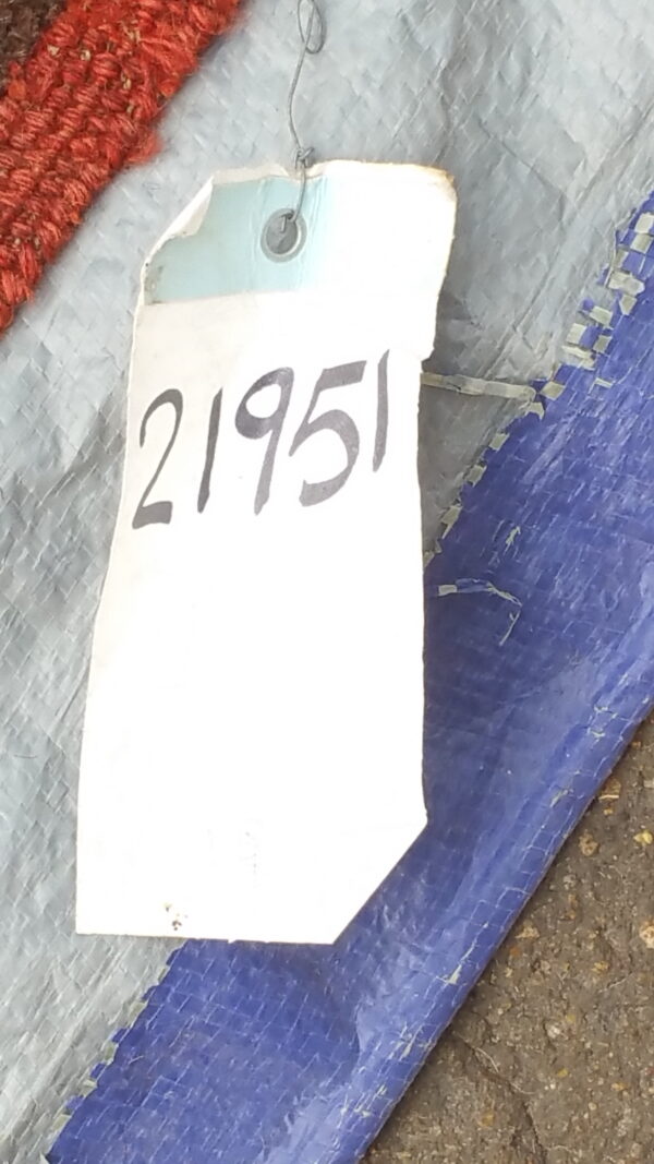 Close-up of a textured red rug edge next to a white tag marked with the number 21951.